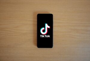 Smartphone with TikTok app displayed on black screen against a wooden background.